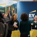 Smiling people standing and talking in front of a colorful wall with EY logo