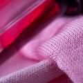 A close-up image of pink woven fabrics and a red bottle of fabric dye.