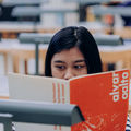 A student's face peaking behind a book while reading in a university library.