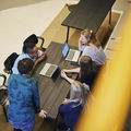 A group of five students discussing with laptops photographed from above.