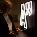 A student scrolling an ipad by an Aalto University logo neon sign.