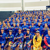 Image of lots of students wearing blue overalls and making a handsign for their guild