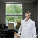 man standing in a storage in front of the window, wearing a white laboratory coat, smiling