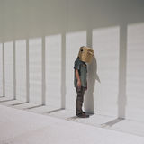 Still from the film Like Shadows Through Leaves, 2021. A figure stands next to a minimalist wall wearing a cardboard bird mask