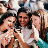 Three students looking at a smartphone screen and smiling at a graduation party. Photo: Jaakko Kahilaniemi / Aalto University