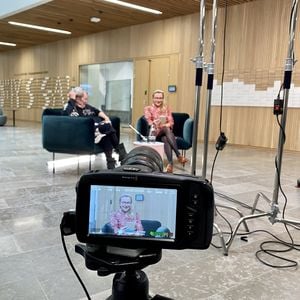 Filming the Back to Work Sessions series. This photo is capturing speakers Hilkka Olkinuora and Hertta Vuorenmaa through a camera lens while they are sitting and discussing next to each other in green chairs.
