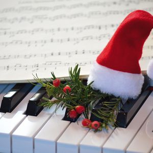Kauneimmat joululaulut -tapahtuman mainoksessa pieni tonttu istuu pianon näppäimistön päällä, taustalla partituurivihko