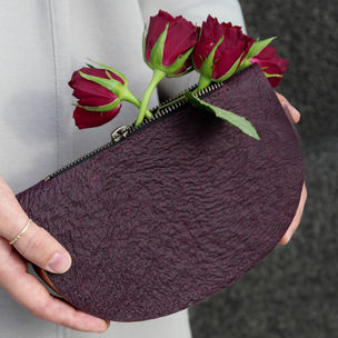 A purse made of leather-like material created from flower waste, red roses stand out from the purse 