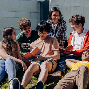 A group of students sitting outside on grass and reading.