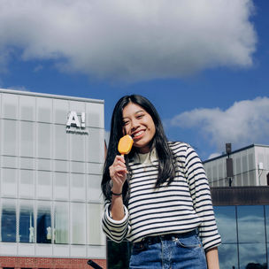 A student eating a yellow ice cream in fron of Aalto University campus.