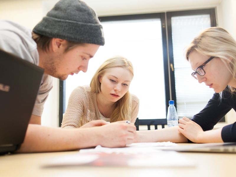 Three Aalto University students are doing group work by writing on paper together.