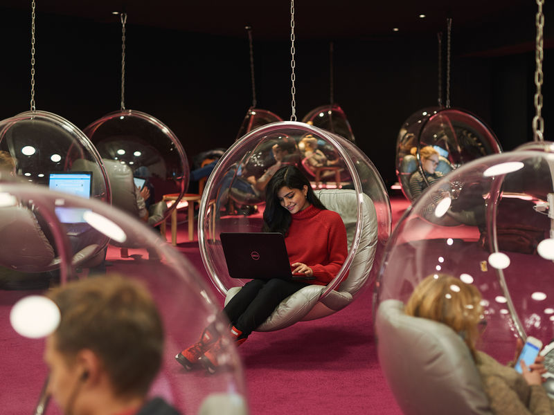 Opiskelija istumassa kupla muotoisessa tuolissa Aalto-yliopiston kirjastolla.