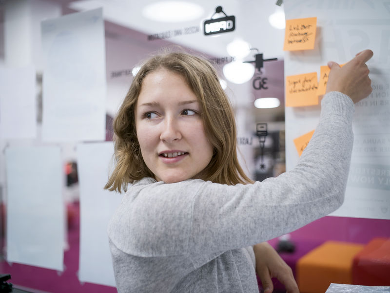 Aalto University student putting post-it notes on a glass wall.