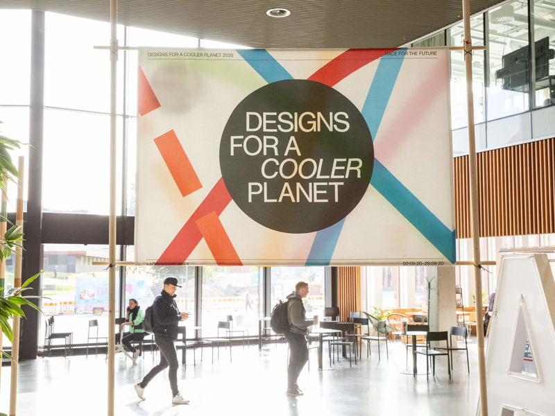 Large banner of the Designs for a Cooler Planet event with a few people walking around it