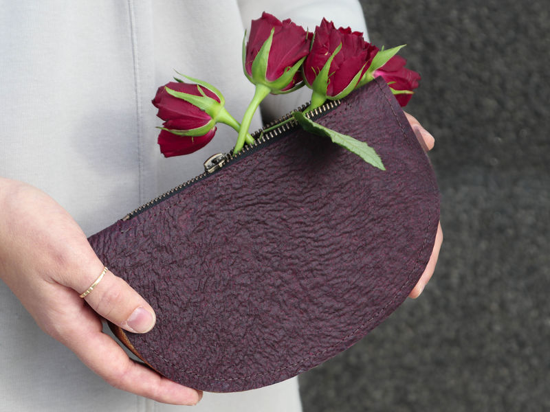 Colour photo showing a dark brown/aubergine coloured clutch purse held in two hands with Roses coming out of the zippered top