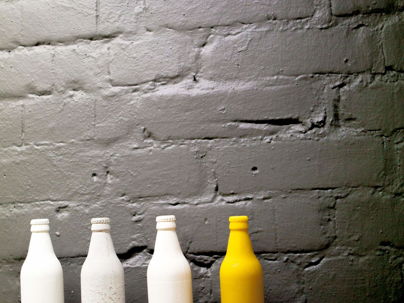 Three white and one yellow painted bottle against a gray brick wall