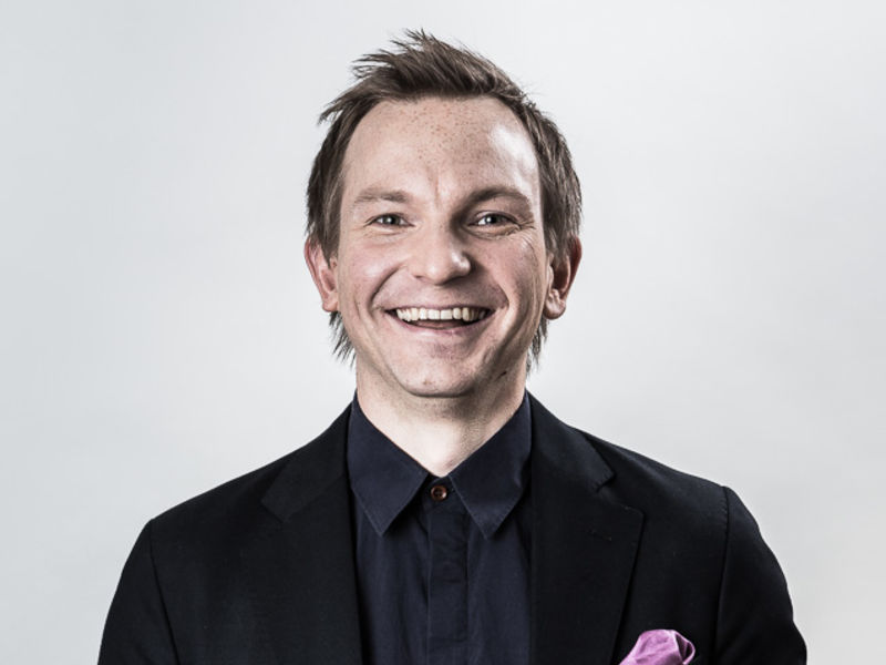 Peter Kenttä in a black blazer and black shirt, smiling towards the camera.