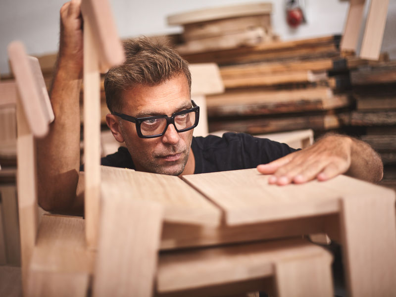 Man looking at a wooden chair, holding it  