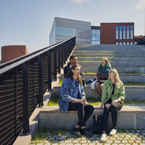 Four people sitting on stairs outside on campus in sunlight