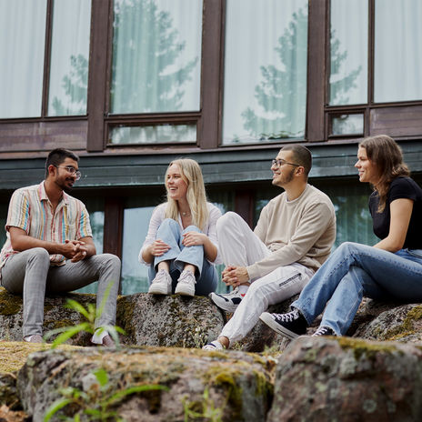Four Aalto University students sitting outside on rocks and talking