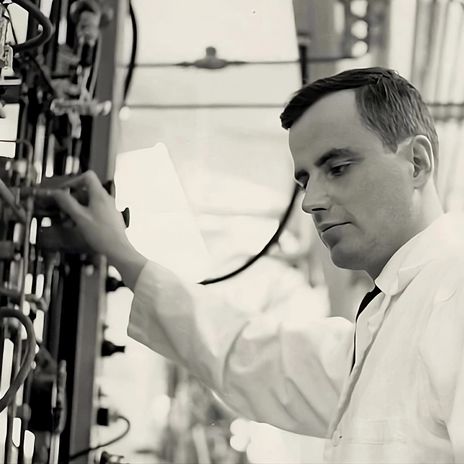 A man in a black and white photo adjusts knobs on a piece of large equipment.