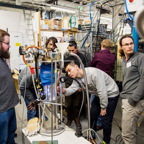 A group of seven researchers observe a complex piece of machinery in the center of the photo.