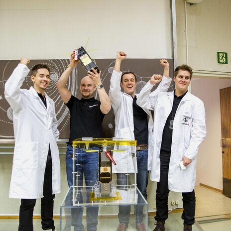 Neljä ihmistä esittelee iloisena satelliittia.