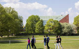 Seven Aalto University students walking on campus on a sunny summer's day. University buildings and lots of trees in the background. Photo: Mikko Raskinen / Aalto University.