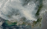 A satellite image of Borneo and part of Malaysia covered by plumes of smoke from fires. The many fires are marked on the map as red dots.