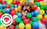 A person peeks through colourful balls in a ball pit. I love campus logo badge in the lower left corner.