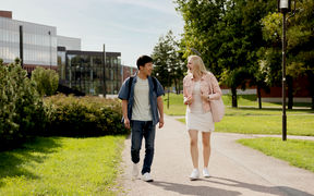 Two students walking on a sunny path by the Väre building