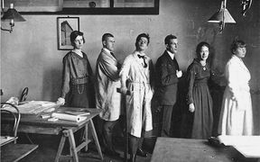 Vuoden 1921 arkkitehtiopiskelijoita poseeraa opetustiloissa jonomuodostelmassa mustavalkoisessa kuvassa