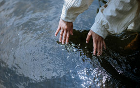 Hands touching the surface of the rippling water.