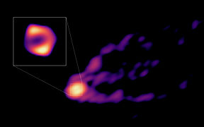 Teleskooppiverkoston ottama kuva galaksin M87 mustan aukon varjosta ja suihkusta. 