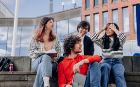 four students sitting outside infront of the Väre building in Otaniemi