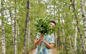 A young person smiles from behind a raised birch branch in front of their face