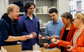 Three men in blue shirts and two women in orange jackets talking and assessing ceramic cubes