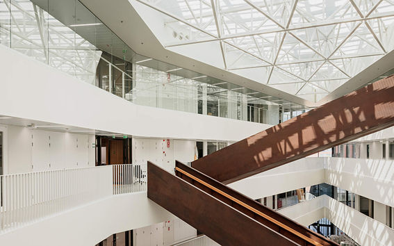 Väre building in the campus. Inside shot of natural light filled dark wood staircase criss-crossing in white surroundings. Light through skylights. Photo by Aalto University / Tuomas Uusheimo