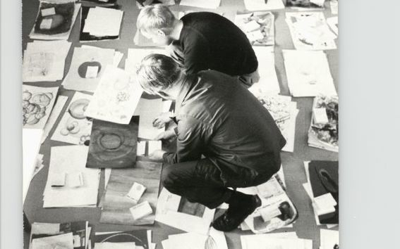 Kolme henkilöä tutkii lattialle pinottuja piirustuksia Taideteollisessa korkeakoulussa 1960-luvulla.. Kuva: Aalto-yliopiston arkisto.