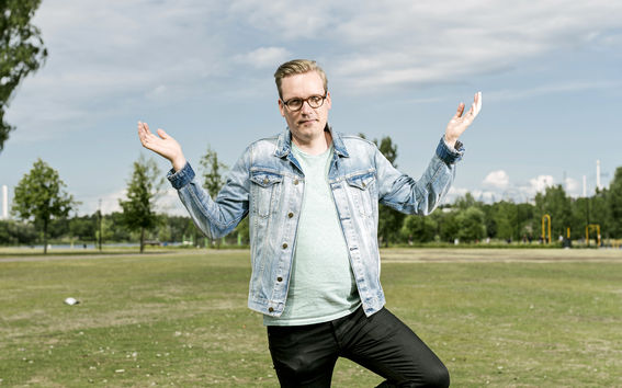 Professori Tuukka Saarimaa seisomassa tyhjällä nurmikentällä, joka sijaitsee Helsingin keskustassa Oodi-kirjaston ja musiikkitalon välisellä puistoalueella. Kuvaaja: Jaakko Kahilaniemi.
