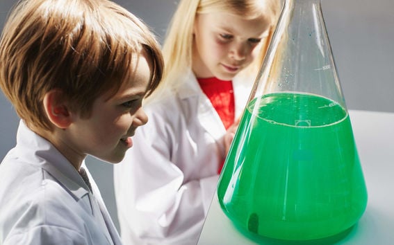 Poika ja tyttö valkoisissa laboratoriotakeissaan ihmettelevät vihreää nestettä laboratoriomaljassa