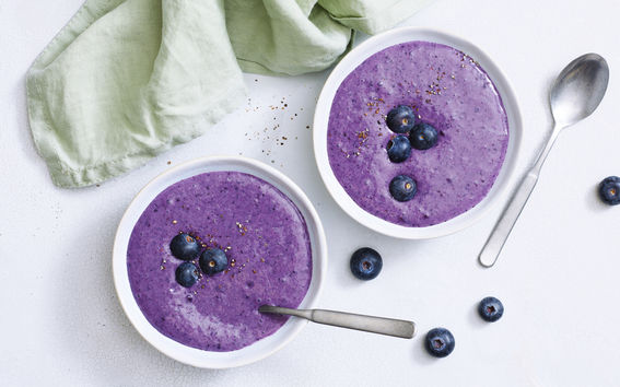 Two bowls of blueberry porridge and a green kitchen towel.