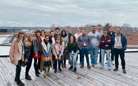 19 students posing with smiles at the School of Business rooftop terrace. 