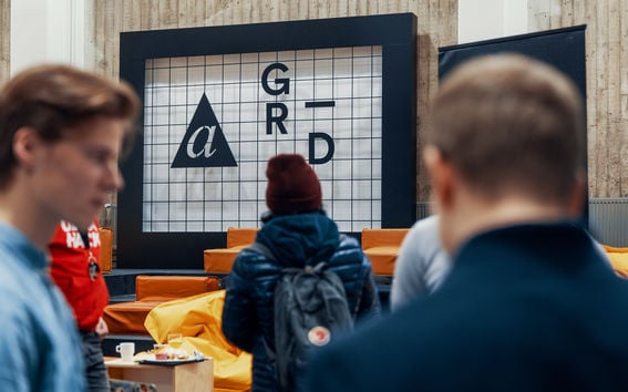 three men talking to each other in the foreground, while another person with back turned looks at the A Grid sign on the background