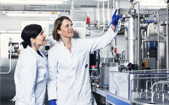 Two lab-coated women in a laboratory looking at pipes.