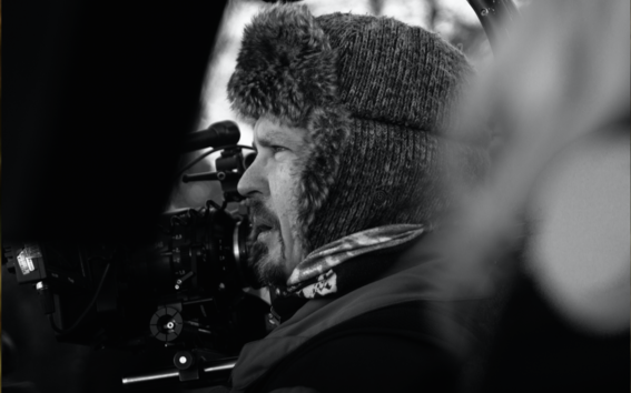 Mies kuvaa elokuvakameralla talvella ulkona, lämmin talvihattu päässään ihmisten seassa. Hänestä näkyy lähikuvassa vain profiili.