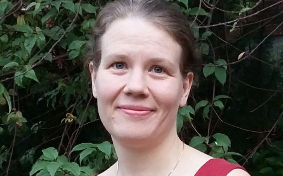 Kuva hymyilevästä Sanna-Liisa Sihto-Nissilästä punaisessa hihattomassa kesäpaidassa, taustalla pensasaita.