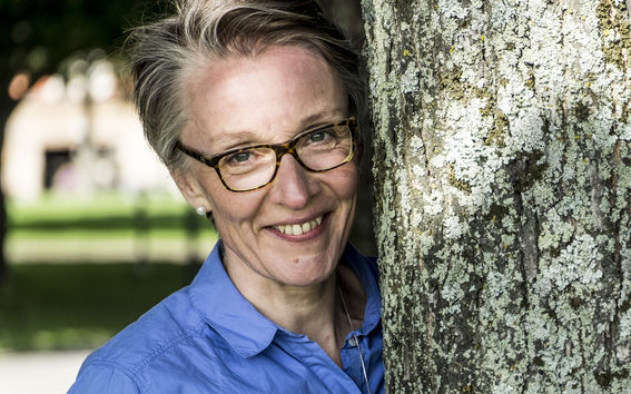 Kuva Leni Grünbaumista. Henkilö nojaa puunrunkoon sinisessä rennossa kauluspaidassaan.