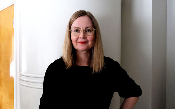 Arkkitehti Anne Tervo väitteli maaliskuussa 2021. Tervo kuvassa mustassa mekossa, taustalla vaalea uuni ja harmaata seinää.