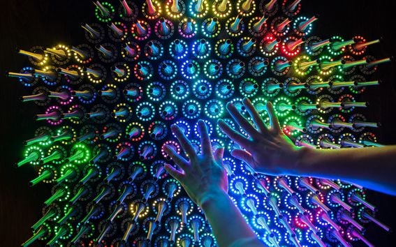 InteraktiiQuantum Garden on interaktiivinen elektroninen valotaideteos, jota koskettamalla teoksen värit muuttuvat. Tummasävyisessä kuvassa kaksi kättä kurkottaa eriväristen valoantureiden päälle.